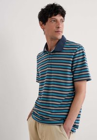Cămașă polo în dungi cu guler bleumarin, având dungi orizontale albastre, teal, gri și crem, mâneci scurte și o închidere cu nasturi.