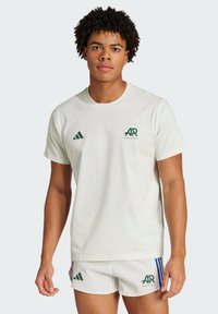 Hvid bomulds-T-shirt med grønt "AR" logo og tre striber på skulderen, parret med hvide shorts og grønne accenter.