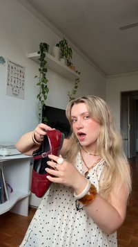 Rdeče lakirane čevlje z črnimi akcenti, ki imajo trak in zaponko. Čevlji imajo zaobljen nos in ravno podplat.
