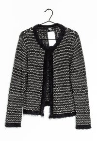 Cardigan de punto texturizado en blanco y negro con ribete suave en el cuello, los puños y el dobladillo, colgando de una percha negra con una etiqueta blanca en blanco.