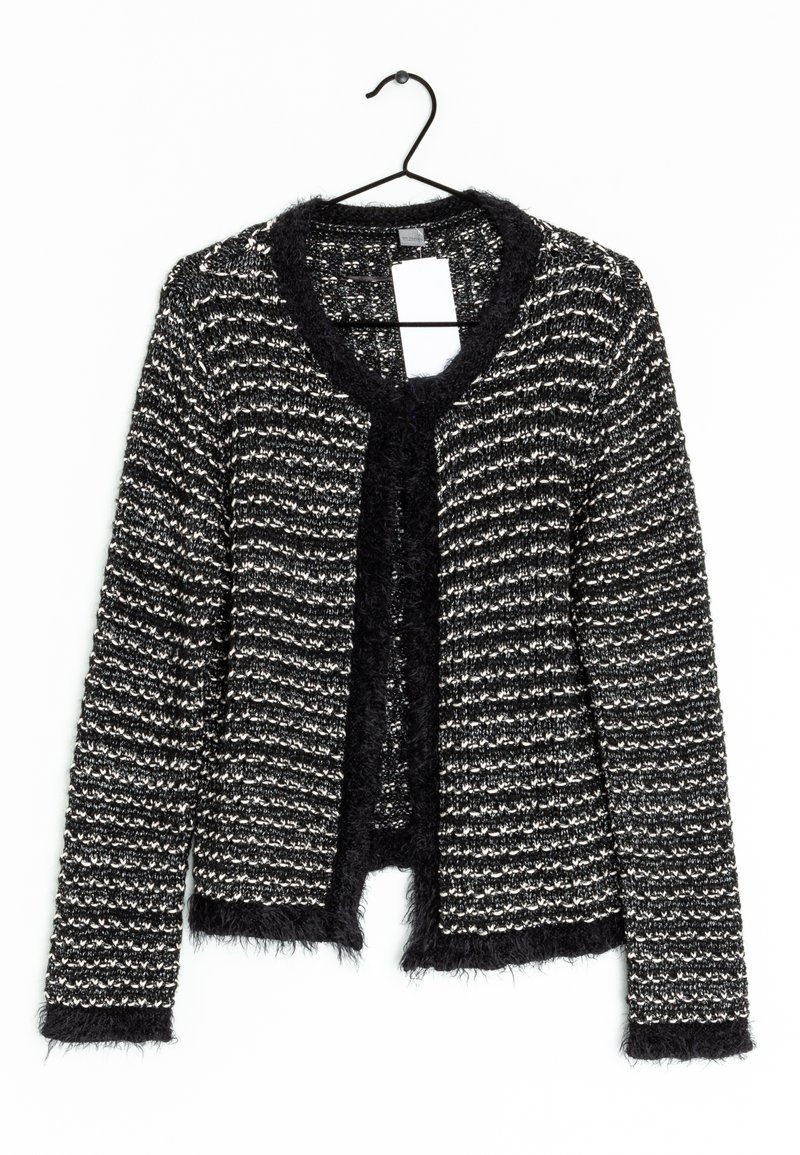 Cardigan de punto texturizado en blanco y negro con ribete suave en el cuello, los puños y el dobladillo, colgando de una percha negra con una etiqueta blanca en blanco.