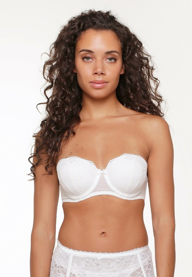 Witte strapless beha met kantdetails, zachte cups voor ondersteuning, golvende randen en een centrale strikaccent. Gladde stof en doorschijnende band eronder.