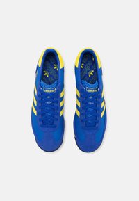 Blauwe sportschoenen met gele accenten, voorzien van een bovenwerk van mesh en suede, drie strepen en een geperforeerde binnenzool.