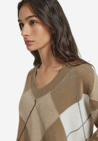 V-Ausschnitt-Pullover in Braun, Creme und Grau mit Rautenmuster; Stricktextur; lockere Passform; mit geripptem Kragen und Saum.