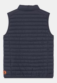 Gilet imbottito senza maniche di colore blu navy, realizzato in tessuto trapuntato, con colletto alto e una toppa con logo sul lato sinistro in basso.