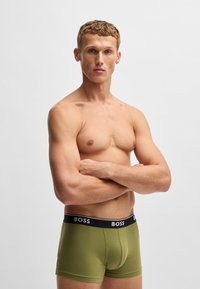 Zöld pamut boxer alsónadrág fekete elasztikus derékkal, amelyen a "BOSS" logó látható. A modellen semleges kifejezés látható, karjait összehúzta.