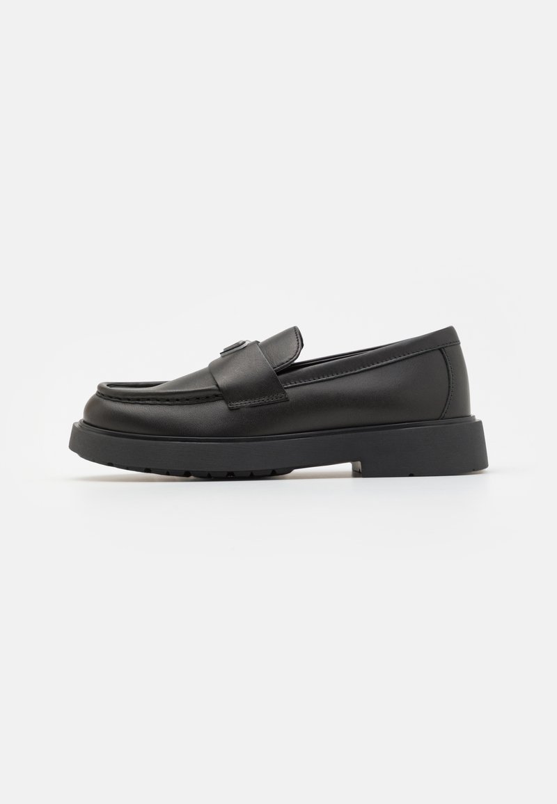 Black leather loafers with a rounded toe, stitched detailing, a small strap across the front, and a low block heel. Textured rubber sole.