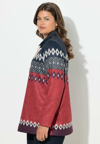 Maglione a maniche lunghe caratterizzato da una combinazione di colori blu e rosso, con fantasie geometriche decorative bianche e un colletto con dettaglio a cordoncino.