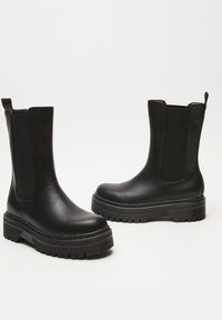 Black leather ankle boots featuring wide elastic side panels, a chunky rubber sole, and a pull tab at the back. Smooth texture throughout.