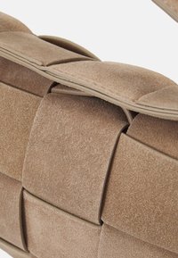 Sac en suède beige présentant un design tissé avec des rectangles rembourrés proéminents. Accentué par des bords lisses et une légère brillance.