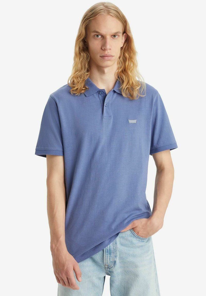 Polo shirt in cotone blu con colletto classico, tre bottoni, maniche corte e un piccolo logo ricamato sul lato sinistro del petto.