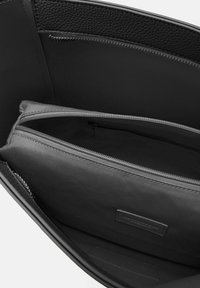 Interno di una borsa in pelle nera con fodera in tessuto grigia, dotata di due scomparti con zip e un dettaglio in pelle texturizzata.