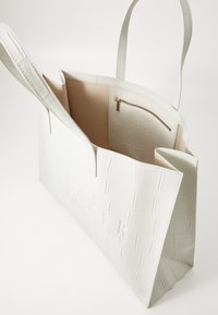 White faux leather tote bag with a textured pattern, open top, and two handles. Interior features a beige lining and a zippered pocket.