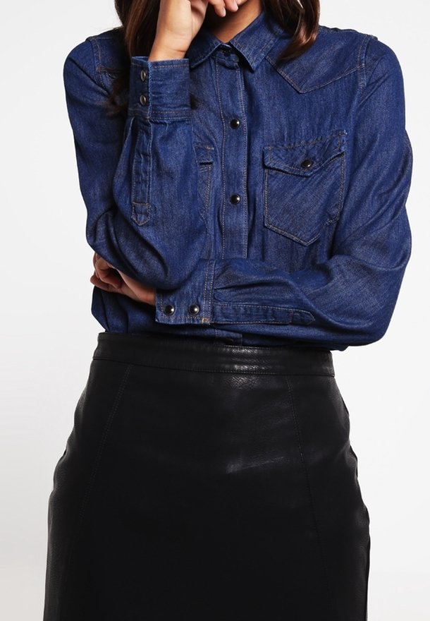 Koszula jeansowa w ciemnym niebieskim kolorze z zapięciem na guziki, dwoma kieszeniami na piersi i podwiniętymi mankietami, połączona z czarną skórzaną ołówkową spódnicą.