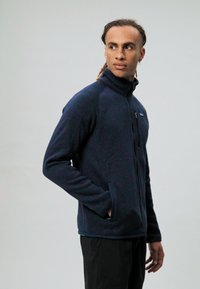 Giacca in pile da uomo navy con colletto alto, zip frontale, tasche laterali, cuciture a contrasto e una toppa del logo sulla parte sinistra del petto.