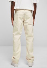 Pantalons en coton beige clair à coupe droite, dotés de deux poches arrière avec des rabats pointus et d'une texture lisse.