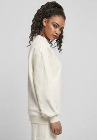 Kremfarget sweatshirt med avslappet passform, rund halsutringning og ribbede mansjetter, laget av mykt stoff. Har en jevn tekstur.