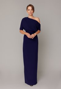 Granatowa sukienka na jedno ramie z dopasowaną talią, zwiewnym dołem i delikatnym drapowaniem. Gładka tekstura, długość do kostek i subtelny połysk.