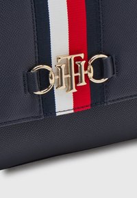 Borsa sintetica navy con finitura textured, caratterizzata da un accento a strisce rosse, bianche e blu e una chiusura con logo dorato.