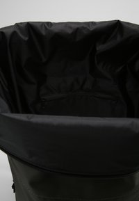 Black backpack interior with a smooth texture, featuring a zipped pocket against a shiny, flexible fabric lining.