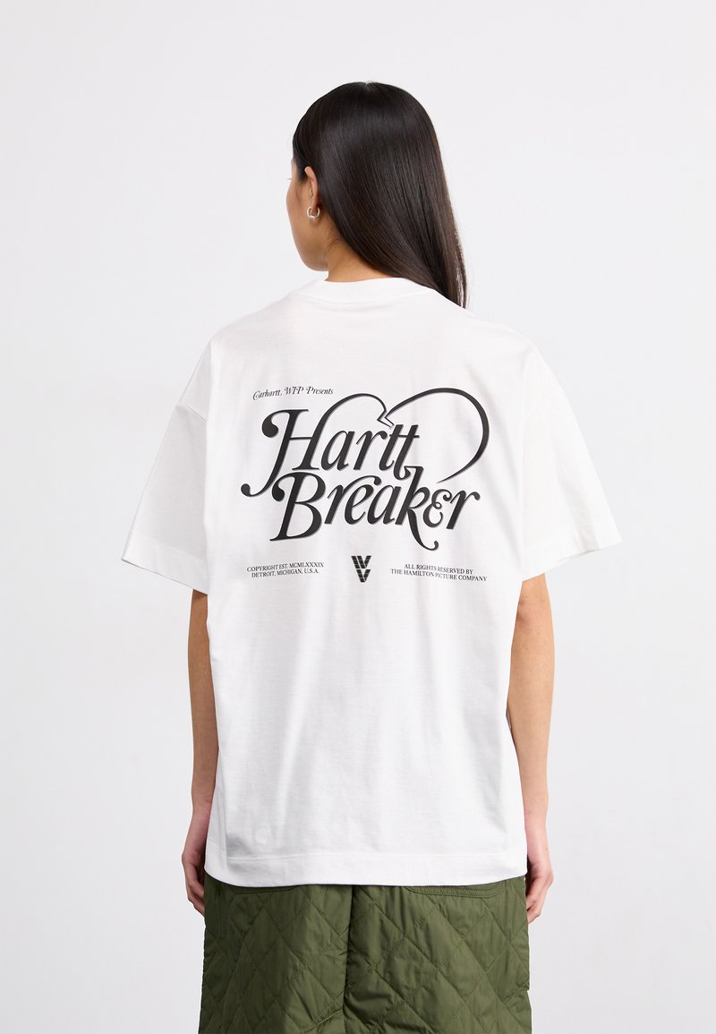 Bílý bavlněný tričko s velkým černým grafickým potiskem na zadní straně, s textem "Hartt Breaker" a uvolněným střihem.