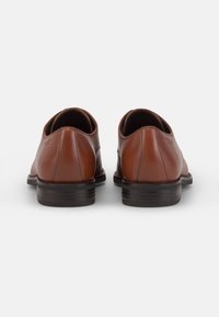 Chaussures en cuir marron avec une texture lisse, un bout arrondi et un talon bas empilé. Le design présente des coutures minimales et une silhouette élégante.