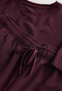 Bordowy zestaw do noszenia w domu wykonany z teksturowanej, prążkowanej tkaniny. Góra ma okrągły dekolt, a dół posiada elastyczny pas z troczkiem.