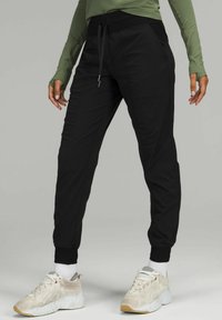 Schwarze Jogginghosen mit schmalem Schnitt, elastischem Bund und Kordelzug. Der Stoff hat eine glatte Textur und verfügt über Seitentaschen.