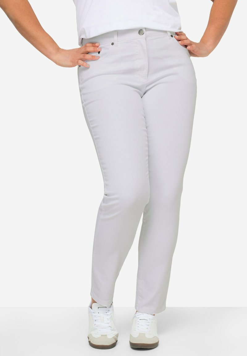 Jean en denim gris clair, avec une coupe slim, des jambes droites, des poches avant et une fermeture à bouton, associés à des baskets blanches.