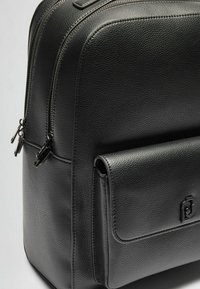 Zaino in pelle nera con finitura testurizzata, scomparti a doppia zip e una tasca frontale con pattina dotata di logo in rilievo. Design compatto e snello.