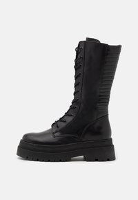 Bottes de combat noires montant jusqu'aux genoux, en cuir lisse, avec un laçage à l'avant, une semelle épaisse en caoutchouc et des détails côtelés à l'arrière.