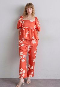 Red floral peplum top with puff sleeves paired with matching wide-leg pants. Made of smooth fabric, features white flower patterns throughout.