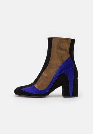 Knöchelhoher Wildlederstiefel mit Blockabsatz in Schwarz, Braun und markanten blauen geschwungenen Akzenten an der Seite und vorne.