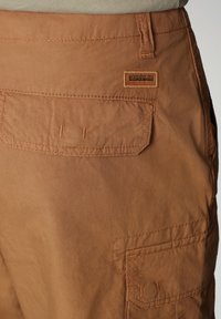 Shorts en tissu marron avec deux grandes poches à rabat, des coutures détaillées et un petit patch rectangulaire avec le logo Napapijri près de la taille.