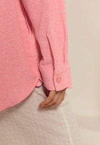Roze overhemden gemaakt van textuurstof, met een afgeronde zoom en manchetten met een enkele knoopdetail. Verstelbare mouwlengte.