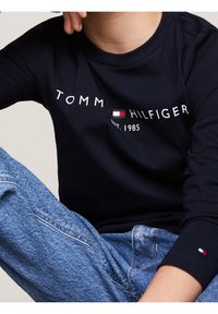Marineblauw T-shirt met lange mouwen met 'TOMMY HILFIGER EST. 1985' opdruk; geribbelde halslijn; gecombineerd met lichtblauwe, vervaagde spijkerbroek.