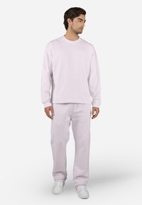 Camisa de manga larga rosa claro y pantalones de chándal a juego, fabricados en algodón suave. Presenta un diseño sencillo con cuello redondo y una marca mínima.