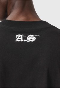 Must must pusa t-särk, millel on valge graafikalogod "A.S" ja "ALL SAINTS" trükitud kaela lähedal selja ülaosas. Lühikesed varrukad.