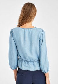 Hellblaues Denim-Bluse mit Dreiviertel-Puffärmeln, gerafftem Bund und rundem Ausschnitt. Weicher Stoff mit einem fallenden Schnitt.