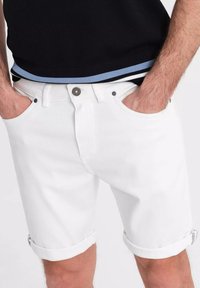 Shorts de mezclilla blanca con dobladillos enrollados, que cuentan con bolsillos frontales estándar y un cierre de botón. La tela tiene una textura suave y un detalle mínimo.
