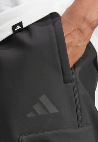 Zwarte sportbroek van Adidas met een gladde textuur, voorzien van een subtiel logo en een zijzak. De tailleband is te combineren met een wit shirt.