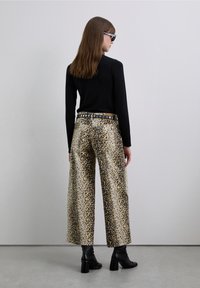 Pantalon à jambes larges imprimé léopard en beige et marron avec une ceinture noire ornée d'accents circulaires, assorti à un haut noir à manches longues et des bottes à talons.