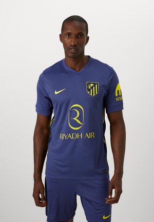 Lilla sporttrøje med korte ærmer, gule detaljer og v-hals. Har et holdlogo, "Riyadh Air" tekst og en tekstureret stofdesign.