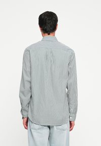 Chemise à manches longues pour homme en blanc et rayures navy. Elle possède un col boutonné, des poignets boutonnés et un empiècement au dos avec un détail de pli.