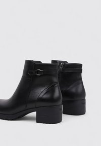 Par de botines de cuero negro con tacones bajos, hebillas laterales y cremalleras sobre un fondo claro.