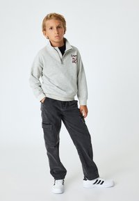 Lys grå zip-up sweatshirt med teksten "Friends in the city", parret med mørke cargo bukser og hvide sneakers med sorte striber.