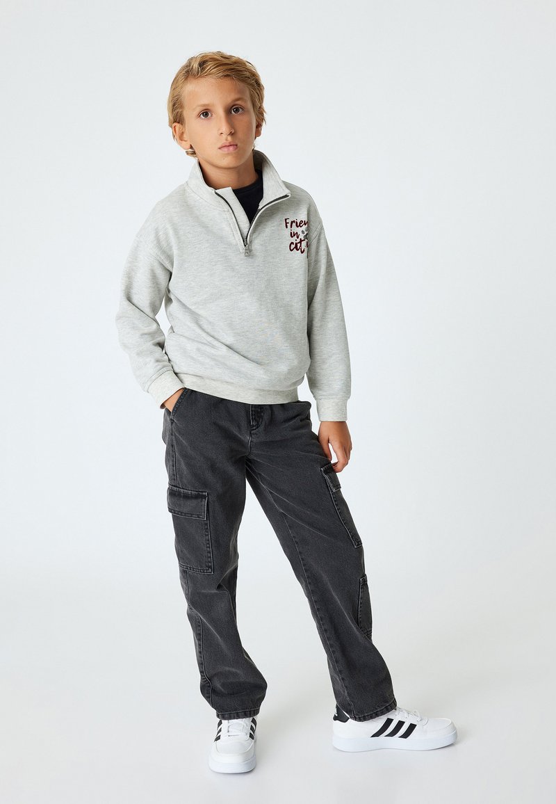 Lys grå zip-up sweatshirt med teksten "Friends in the city", parret med mørke cargo bukser og hvide sneakers med sorte striber.