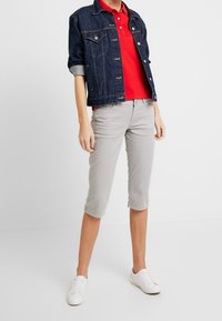 Chaqueta de mezclilla con mangas remangadas, camiseta polo roja, pantalones capri gris claro y zapatillas blancas. Conjunto casual con un ajuste moderno.