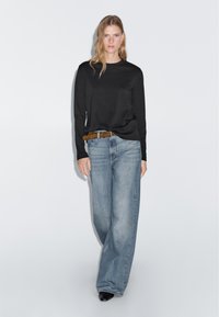 Schwarzes langärmeliges Shirt, kombiniert mit hellblauen weit geschnittenen Jeans und einem braunen Gürtel. Glatter Stoff mit lockerer Passform und minimalistischer Gestaltung.