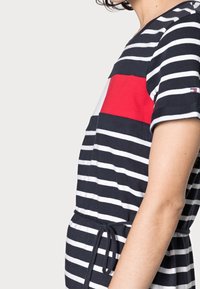 Gestreiftes Kleid in Marineblau und Weiß mit einem roten Akzentpaneel. Hat kurze Ärmel, einen taillierten Bund und einen runden Halsausschnitt.